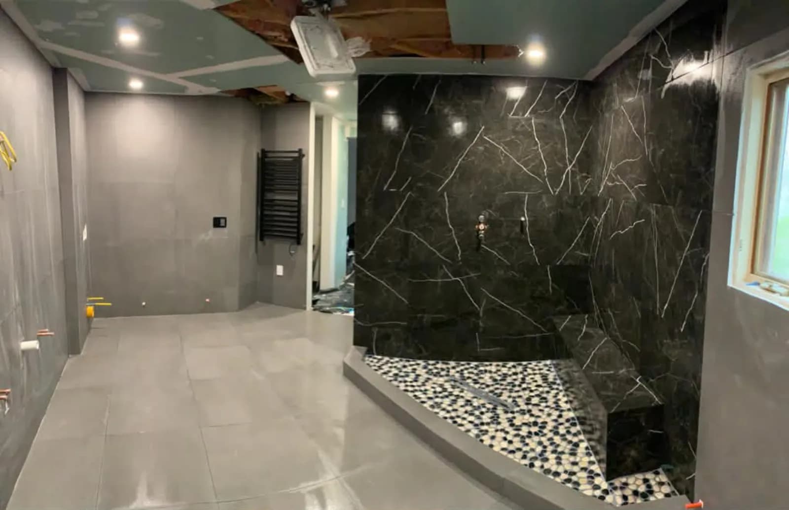 Primary bathroom mid-build with a black marble shower and pebble shower floor