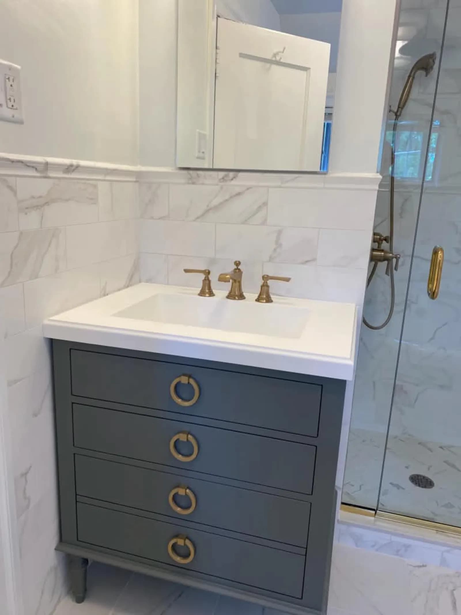 Gray four-drawer vanity with brass ring pulls, brass faucet and marble-look tile
