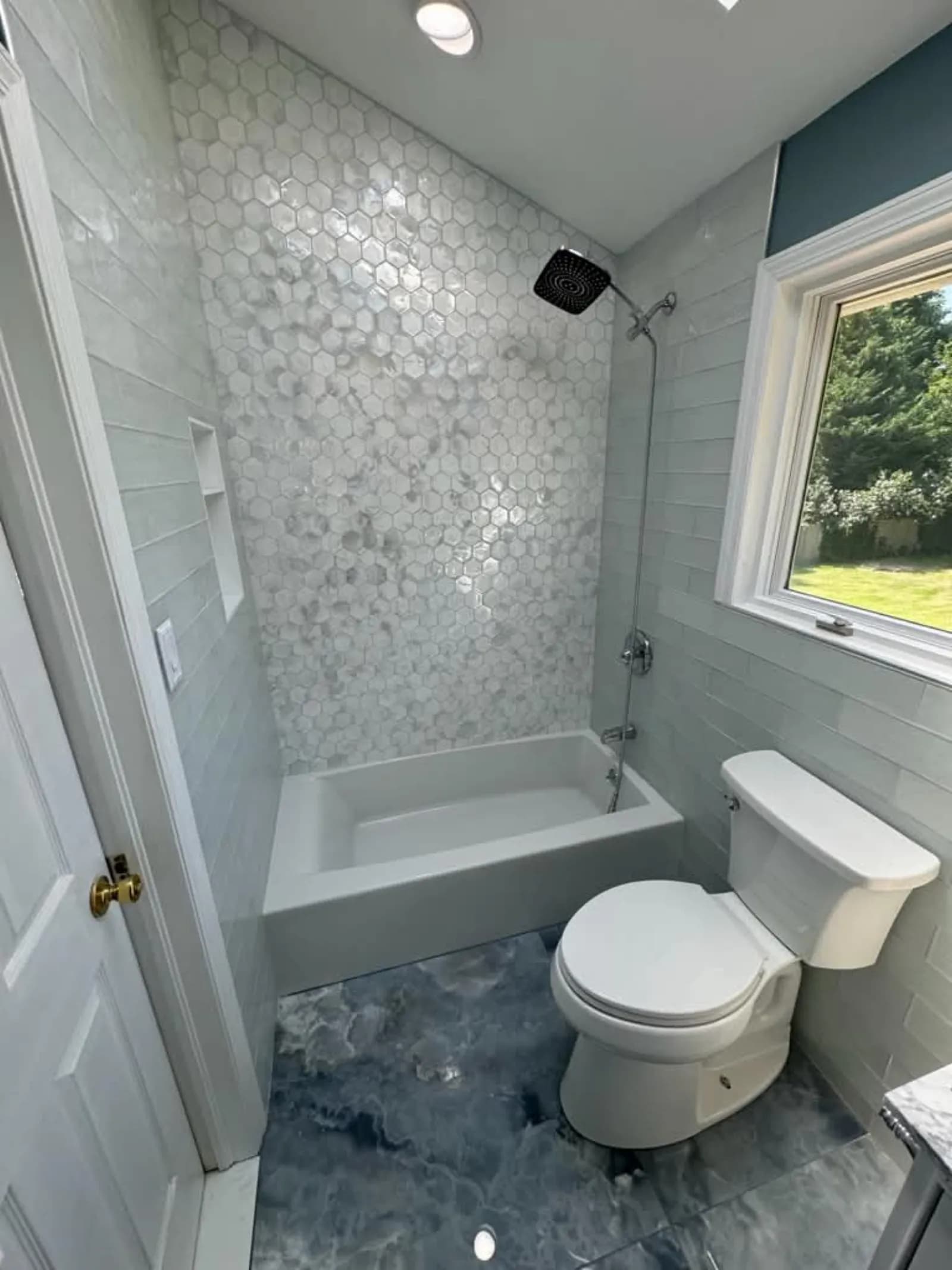 Bathroom with a hexagon tile tub surround, black rain shower head and marbled floor