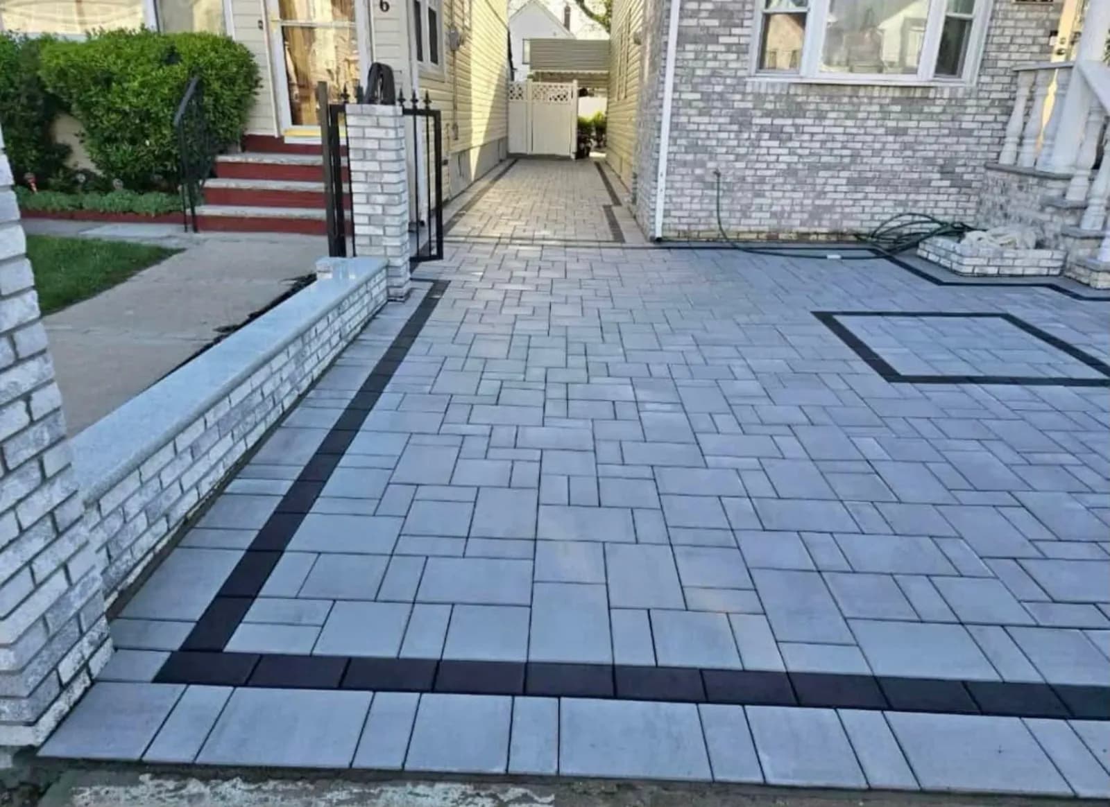 Gray paver driveway with black border inlay and a brick-faced retaining wall
