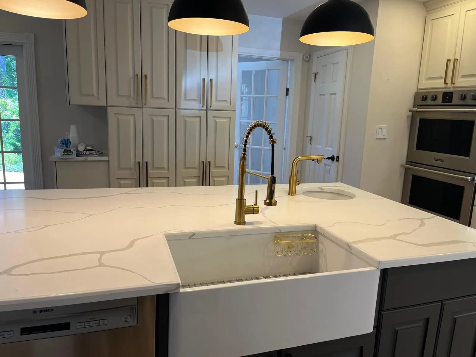 Remodeled kitchen island with veined quartz counter, farmhouse sink and brass faucet
